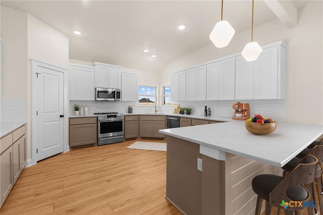 kitchen with stainless steel appliances, a breakfast bar, a peninsula, light wood-type flooring, and pendant lighting