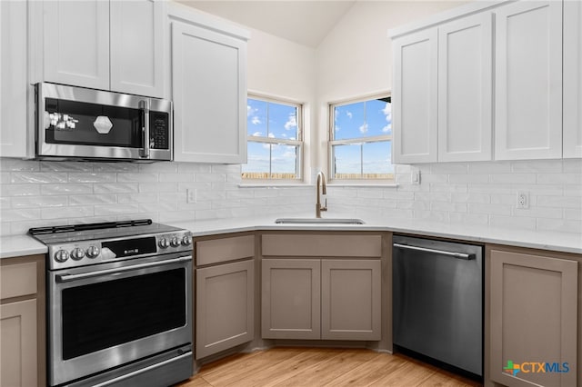 kitchen with gray cabinetry, sink, tasteful backsplash, light hardwood / wood-style floors, and appliances with stainless steel finishes