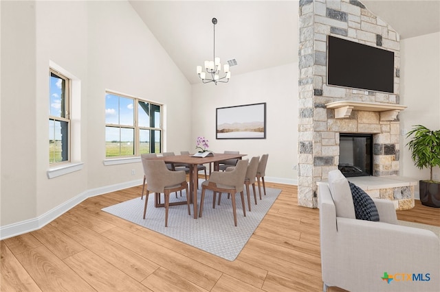 dining space with an inviting chandelier, high vaulted ceiling, light hardwood / wood-style flooring, and a stone fireplace