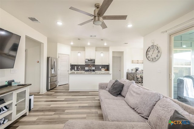 living room with light wood-type flooring, ceiling fan, visible vents, and recessed lighting