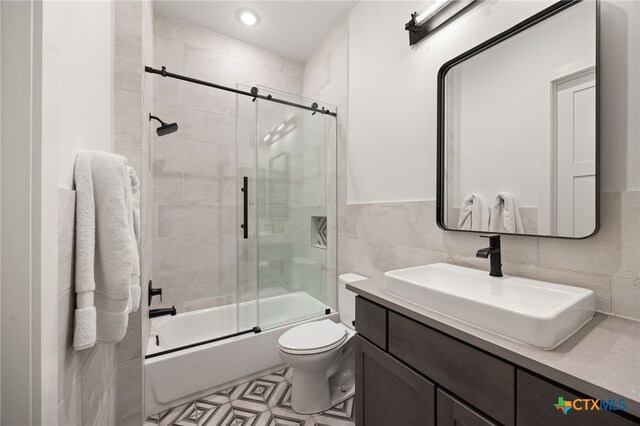 full bathroom with tile walls, shower / bath combination with glass door, toilet, and vanity