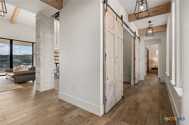 hallway with a barn door, hardwood / wood-style flooring, beamed ceiling, and ornate columns