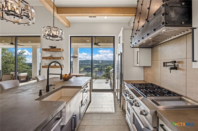 kitchen featuring custom range hood, beam ceiling, sink, stainless steel range, and light hardwood / wood-style floors