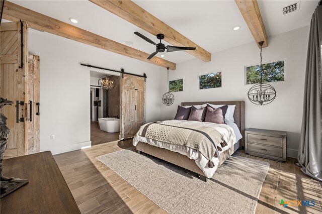 bedroom featuring beamed ceiling, ensuite bath, ceiling fan, a barn door, and dark hardwood / wood-style flooring