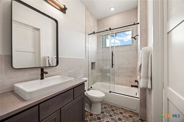 full bathroom with enclosed tub / shower combo, vanity, toilet, and tile walls