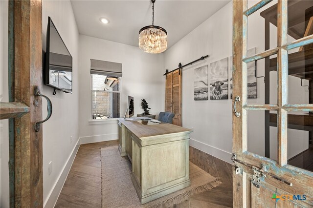 home office featuring a barn door, an inviting chandelier, and dark hardwood / wood-style flooring