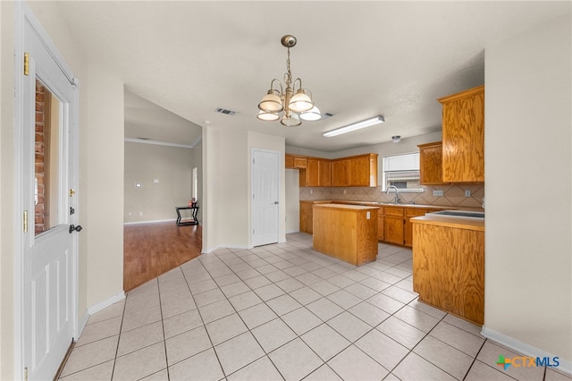 kitchen with light tile patterned flooring, a kitchen island, backsplash, a notable chandelier, and sink