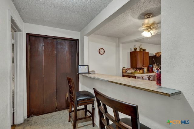 kitchen featuring a kitchen breakfast bar, kitchen peninsula, a textured ceiling, and ceiling fan