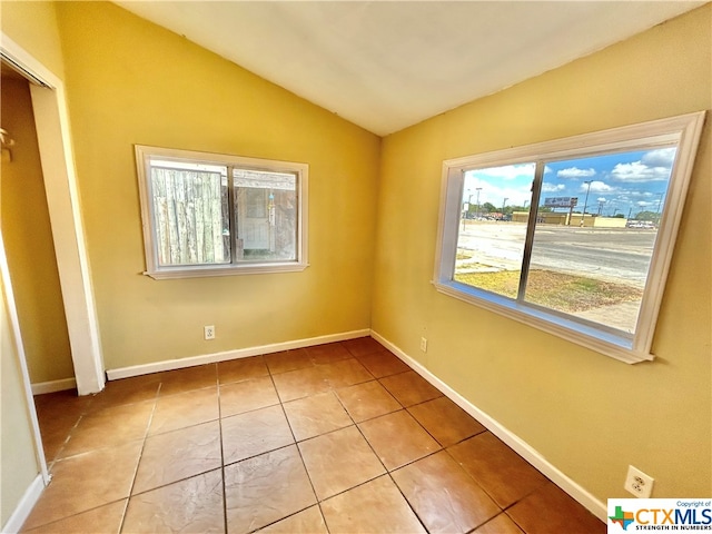 unfurnished room with lofted ceiling, light tile patterned floors, and plenty of natural light