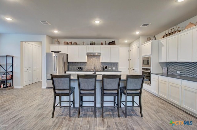 kitchen with stainless steel appliances, an island with sink, light wood-type flooring, and white cabinetry