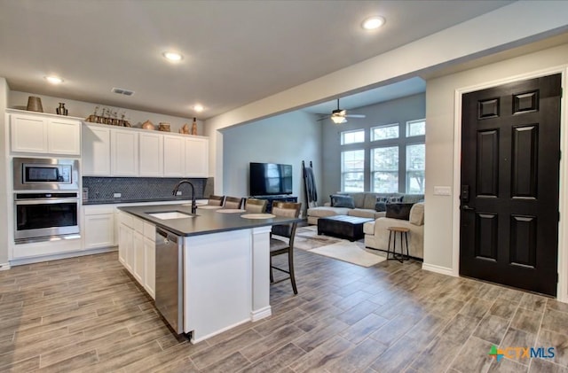 kitchen with sink, a breakfast bar, stainless steel appliances, an island with sink, and white cabinets