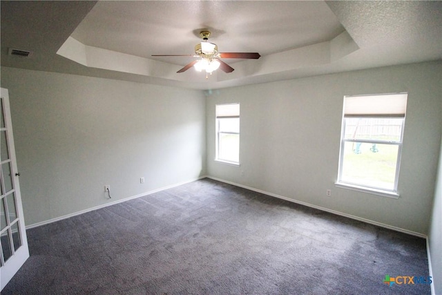 spare room with a tray ceiling, ceiling fan, and dark carpet