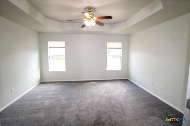 spare room featuring a tray ceiling, dark carpet, a wealth of natural light, and ceiling fan