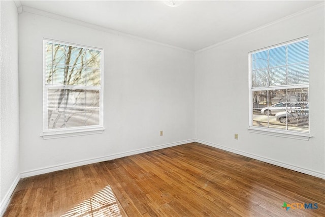 empty room featuring crown molding, baseboards, and hardwood / wood-style flooring
