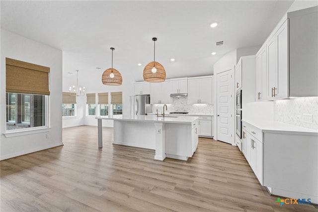 kitchen featuring a center island with sink, hanging light fixtures, light wood-type flooring, appliances with stainless steel finishes, and white cabinetry