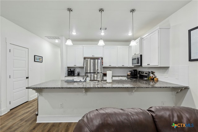 kitchen featuring visible vents, appliances with stainless steel finishes, open floor plan, dark stone countertops, and a peninsula