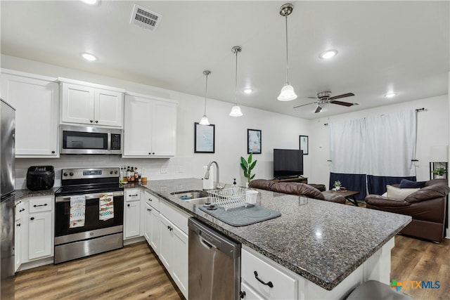 kitchen with visible vents, appliances with stainless steel finishes, open floor plan, a sink, and a peninsula