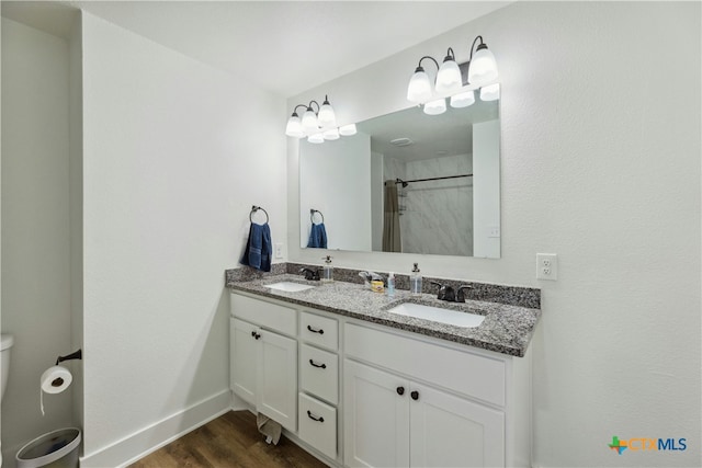 full bath with double vanity, wood finished floors, a sink, and baseboards