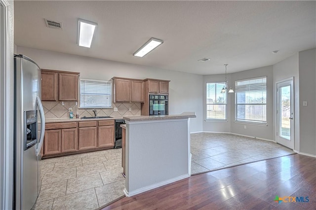 kitchen featuring stainless steel refrigerator with ice dispenser, backsplash, sink, a notable chandelier, and hanging light fixtures