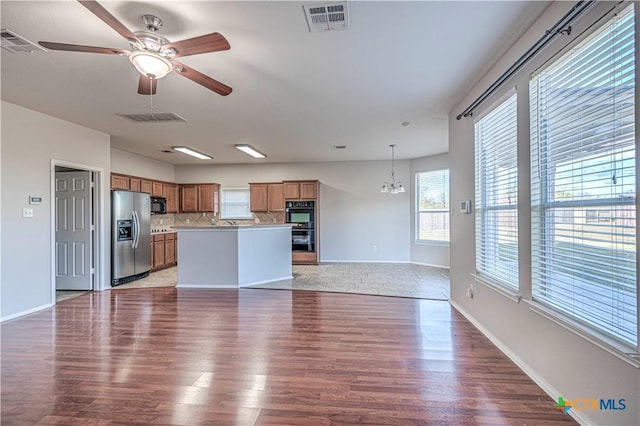 kitchen with tasteful backsplash, black appliances, light hardwood / wood-style flooring, a center island, and hanging light fixtures