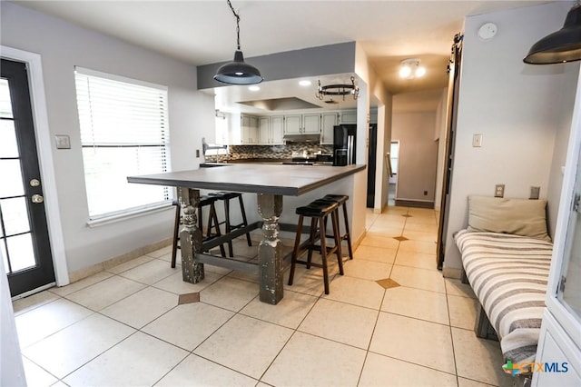 kitchen featuring dark countertops, decorative backsplash, under cabinet range hood, light tile patterned floors, and hanging light fixtures
