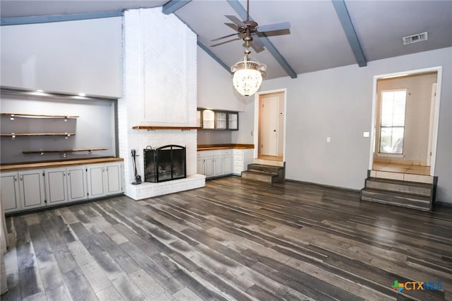 unfurnished living room featuring dark wood-style floors, visible vents, a ceiling fan, beamed ceiling, and a brick fireplace