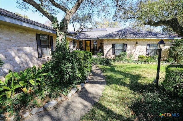 exterior space featuring brick siding, solar panels, and a front lawn