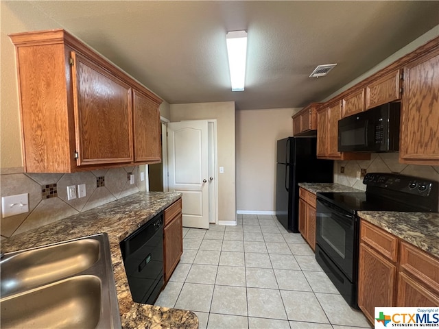 kitchen featuring sink, black appliances, dark stone counters, light tile patterned floors, and decorative backsplash