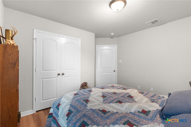 bedroom with baseboards, a closet, wood finished floors, and visible vents