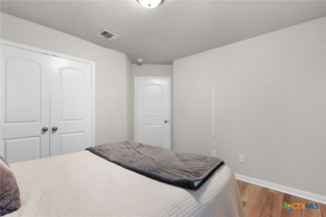 bedroom with baseboards, visible vents, wood finished floors, and a closet