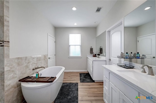 1512 Stonecrest Dr, Granite Shoals, TX 78654 - full bathroom featuring a soaking tub, two vanities, wood finished floors, tile walls, and recessed lighting
