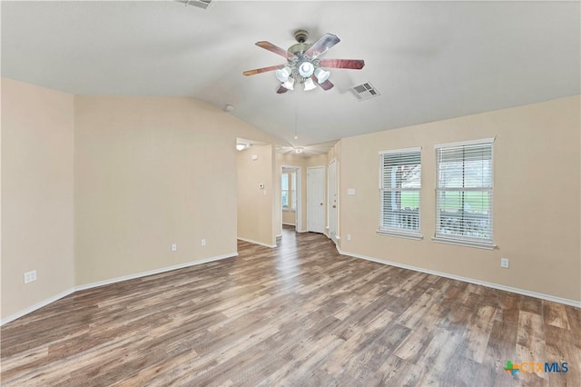 empty room featuring lofted ceiling, wood finished floors, visible vents, baseboards, and a ceiling fan