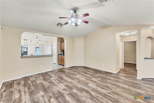 unfurnished living room featuring arched walkways, wood finished floors, visible vents, and lofted ceiling