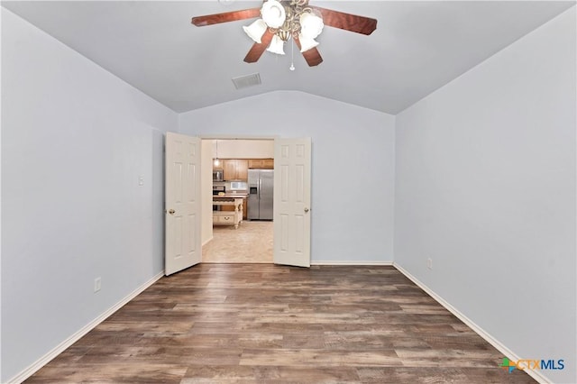 empty room with visible vents, vaulted ceiling, baseboards, and wood finished floors