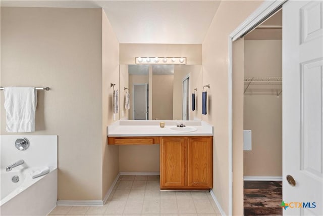 full bathroom featuring a walk in closet, vanity, baseboards, and a bath