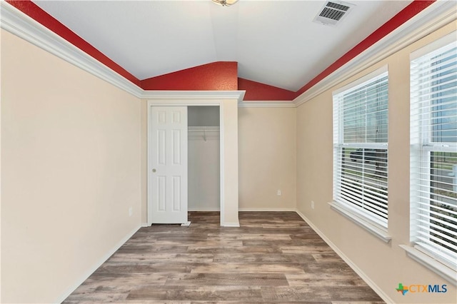 unfurnished bedroom with a closet, visible vents, vaulted ceiling, wood finished floors, and baseboards