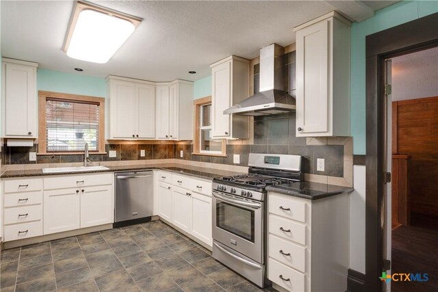 kitchen featuring sink, wall chimney exhaust hood, stainless steel appliances, tasteful backsplash, and white cabinets