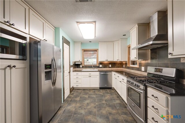 kitchen featuring appliances with stainless steel finishes, backsplash, sink, wall chimney range hood, and white cabinets