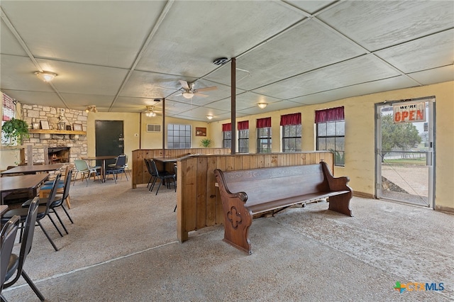 interior space with a stone fireplace, carpet floors, a drop ceiling, and ceiling fan