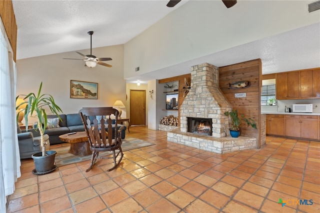 living room with a stone fireplace, light tile patterned floors, a textured ceiling, and ceiling fan