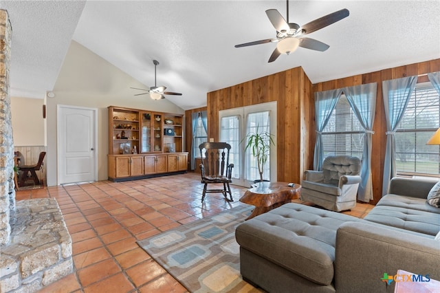 living room with tile patterned floors, wood walls, vaulted ceiling, a textured ceiling, and ceiling fan