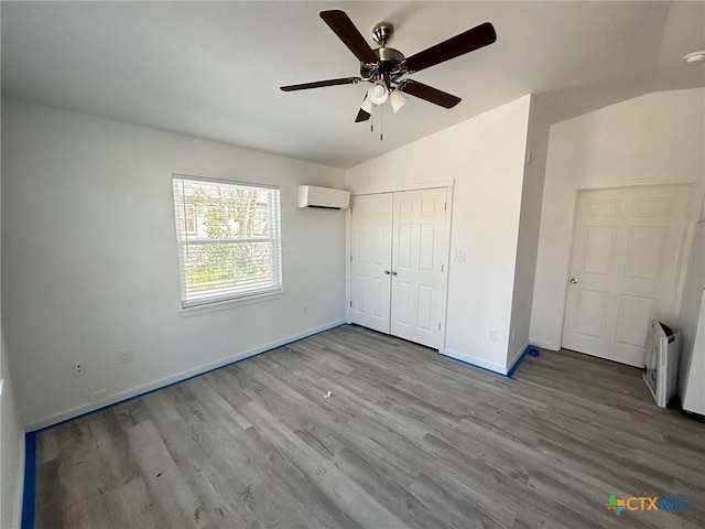 unfurnished bedroom featuring a wall unit AC, ceiling fan, vaulted ceiling, baseboards, and wood finished floors