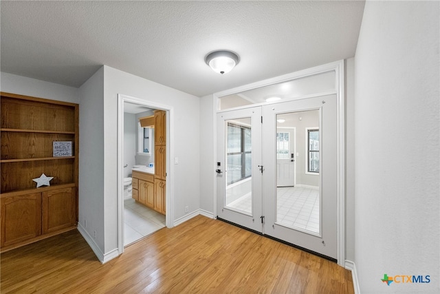 interior space featuring french doors, light wood-type flooring, and a textured ceiling