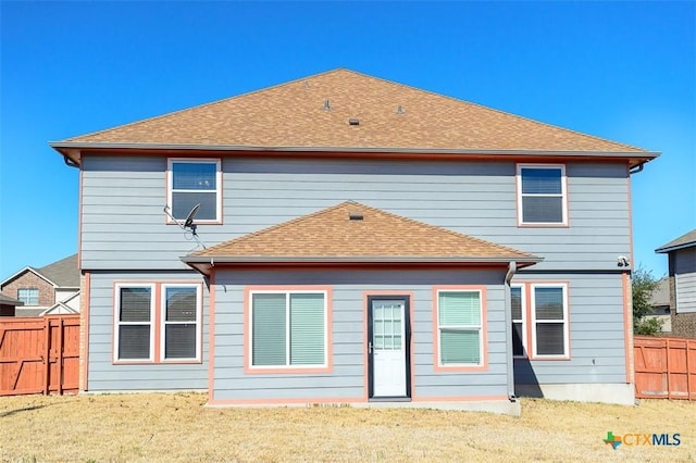 back of property featuring a lawn, roof with shingles, and fence