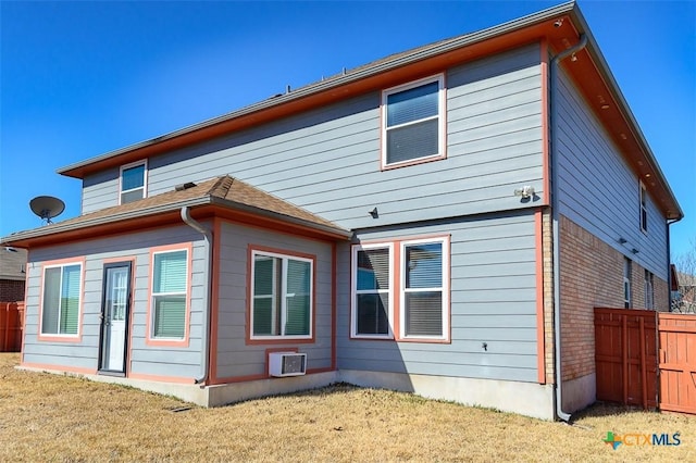 back of house featuring a lawn, a wall mounted air conditioner, and fence