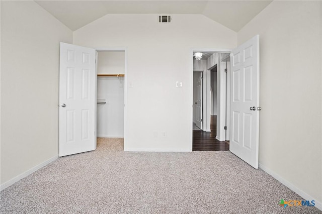 unfurnished bedroom featuring a walk in closet, a closet, carpet floors, and lofted ceiling