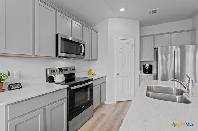 kitchen with gray cabinetry, sink, stainless steel appliances, and light stone countertops