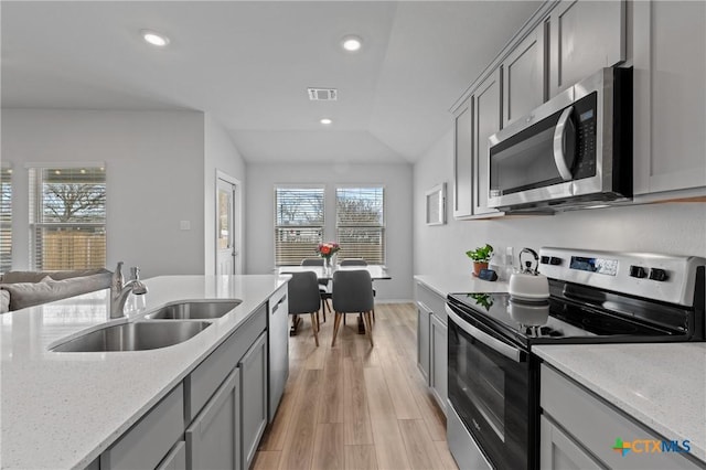 kitchen featuring vaulted ceiling, sink, light stone counters, light hardwood / wood-style floors, and stainless steel appliances