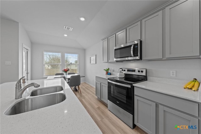 kitchen with lofted ceiling, sink, light hardwood / wood-style flooring, appliances with stainless steel finishes, and light stone countertops