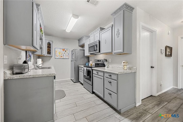 504 Surghnor St, Belton, TX 76513 - kitchen featuring appliances with stainless steel finishes, gray cabinetry, wood finish floors, and a textured ceiling
